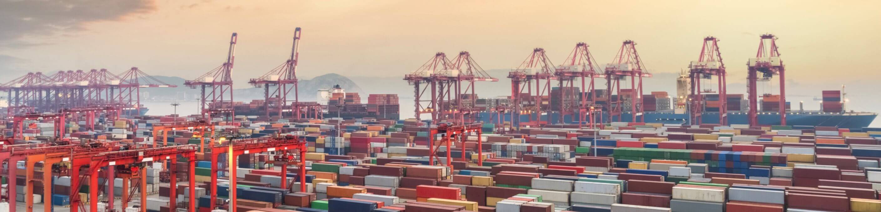 A busy commercial port with many shipping containers and container lifts. 